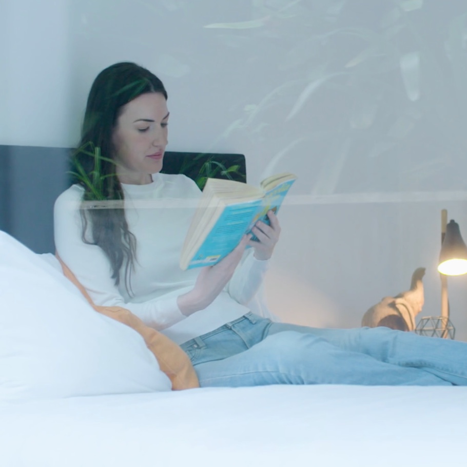 A woman reads a book as she sits on a bed.